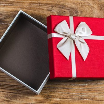 Gift box tied red ribbon with small red hearts printed on it. On old wooden background.